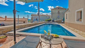 Une piscine avec une table et des chaises, entourée de bâtiments et sous un ciel dégagé.