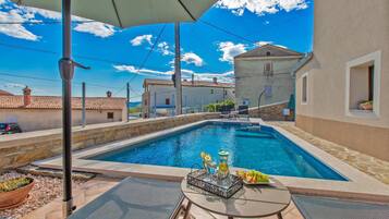 A swimming pool with a table and chairs, surrounded by buildings and a clear sky.
