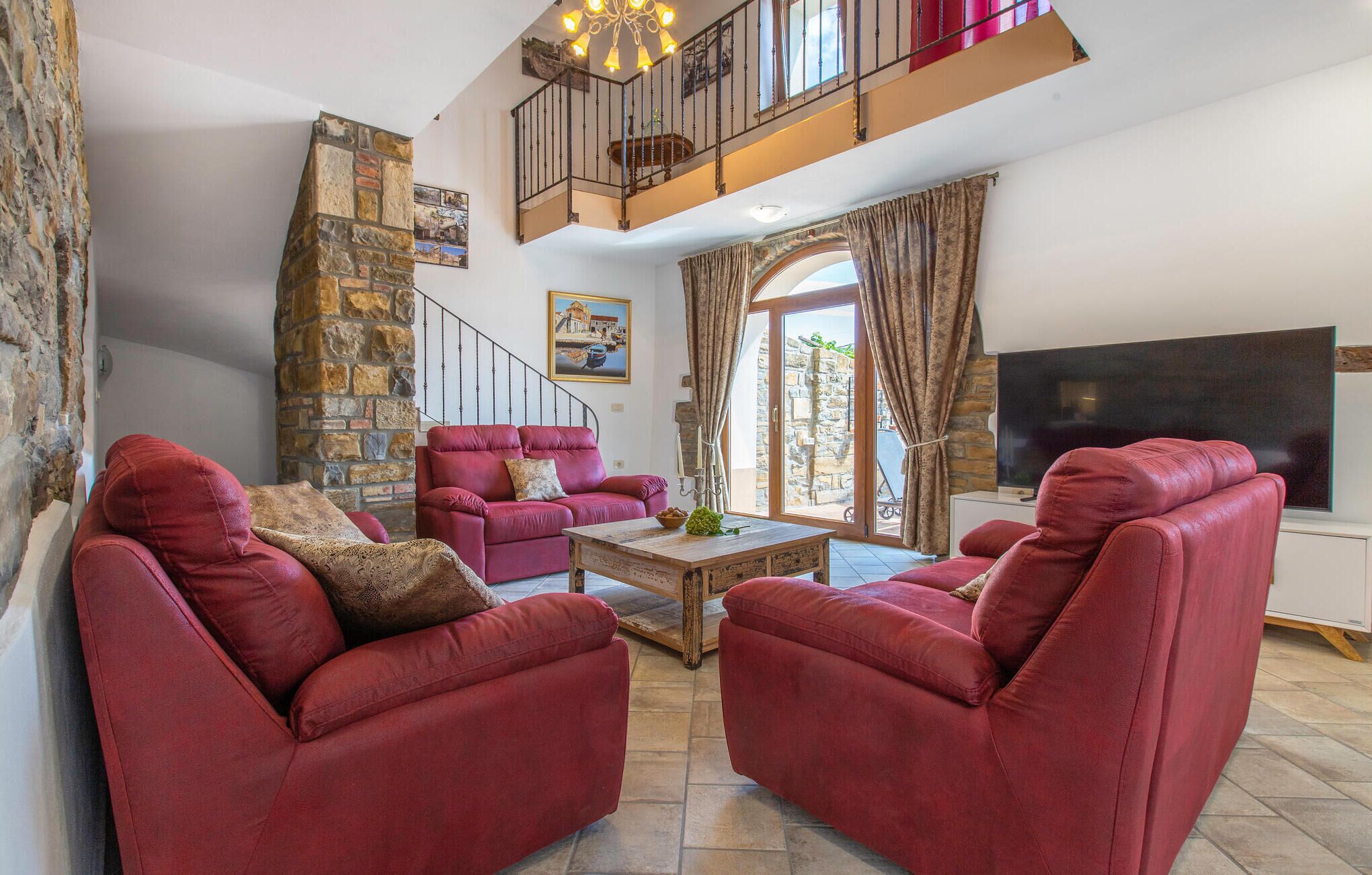 A spacious living room with red leather sofas, a wooden coffee table, and a large TV. A stone wall and staircase are visible in the background.