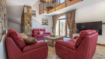 A spacious living room with red leather sofas, a wooden coffee table, and a large TV. A stone wall and staircase are visible in the background.