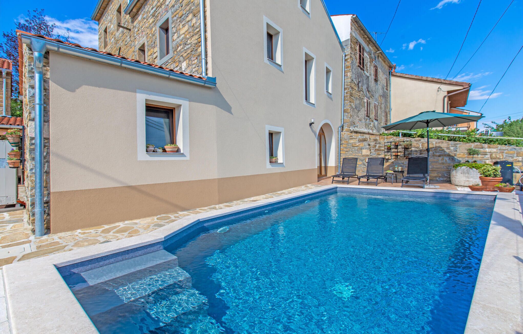 A swimming pool with clear blue water, surrounded by stone walls and a building with multiple windows.