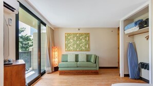 A hotel room with a wooden floor, a green sofa, a bed, a large window, and a wall-mounted air conditioner.