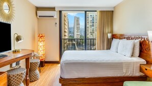 Une chambre d’hôtel avec un grand lit, un bureau avec une chaise, une télévision et une vue sur les grands immeubles depuis un balcon.