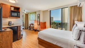 Une chambre d’hôtel comprenant un lit, un bureau avec un micro-ondes, un petit réfrigérateur, une chaise, une table avec une lampe et une grande fenêtre donnant sur l’océan.