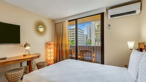 Habitación de hotel con cama, escritorio, silla, mesita pequeña, espejo y vista a la ciudad a través de amplias ventanas.