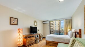 A hotel room with a bed, a TV, a desk, and a balcony with a view of buildings.