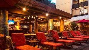 An outdoor seating area with wooden lounge chairs and a bar in the background.