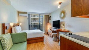 Habitación de hotel con cama, sofá verde, escritorio con televisor de pantalla plana, espejo y ventana con vistas al exterior.