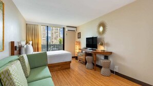 Une chambre d’hôtel avec un lit, un canapé vert, un bureau avec une télévision et une vue sur les immeubles par la fenêtre.