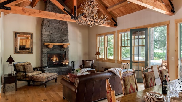 A cozy living room with a fireplace, leather sofa, wooden dining table, and large windows. - Outpost: Granite Ridge Homestead 3093 - Hot Tub! (Teton Village)