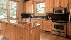 A modern kitchen with wooden cabinets, a granite countertop, stainless steel appliances, and large windows. - Outpost: Granite Ridge Homestead 3093 - Hot Tub! (Teton Village)
