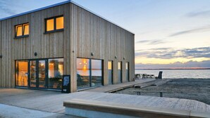 Un edificio moderno de madera con amplios ventanales, una terraza de madera y vista al agua.