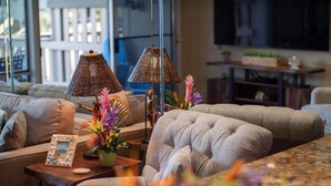 A living room with a sofa, two lamps, a small table with a picture frame and flowers, and a TV in the background.