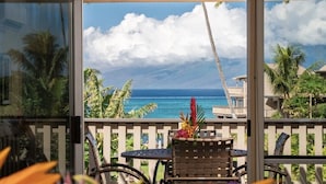 A balcony with a view of the ocean, a table with chairs, and tropical plants.