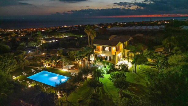 Ein großes, zweistöckiges Haus mit Swimmingpool, umgeben von üppiger Vegetation und Blick auf das Meer im Abendrot.