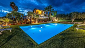 Ein Swimmingpool mit einem gepflegten Rasen, eine Terrasse mit Sitzgelegenheiten und ein Haus im Hintergrund.