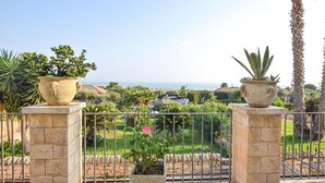 Ein Balkon mit zwei großen Pflanzkübeln, einer Steinmauer und Blick auf das Meer und die Stadt.