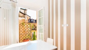 A room with a white table, a chair, a window, and a view of a garden.