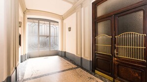 A hallway with a large wooden door, a glass door with a geometric pattern, and a tiled floor.