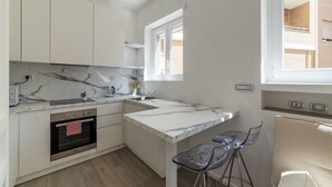 A compact kitchen with a marble countertop, built-in oven, and a small dining area with a clear chair. - GuestHost - Vatican Museums and St. Peter's Basilica! (Roma)