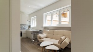 A modern kitchen with white cabinets, a marble countertop, and a built-in oven. There is a beige sofa with a white coffee table and two chairs. - GuestHost - Vatican Museums and St. Peter's Basilica! (Roma)
