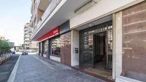 A building with a red sign labeled 'Roma' on the ground floor, a stone-paved sidewalk, and a parked car in the background. - GuestHost - Vatican Museums and St. Peter's Basilica! (Roma)