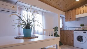 Ett modernt kök med tvättmaskin, träskåp, ett matbord med en krukväxt och ett fönster med tunna, genomskinliga gardiner.