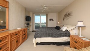 Een slaapkamer met een groot bed, een plafondventilator, een televisie en uitzicht op de stad door het raam.
