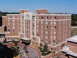 A multi-story brick building with a central courtyard, outdoor seating, and a landscaped area.