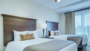 A hotel room with two beds, a large window with curtains, and a ceiling fan.