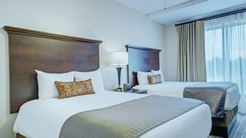 A hotel room with two beds, a large window with curtains, and a ceiling fan.
