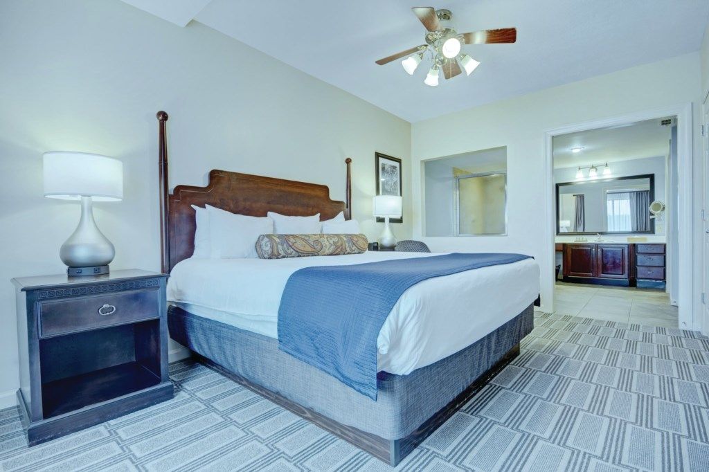 A hotel room with a large bed, a nightstand, a ceiling fan, a bathroom visible through an open door, and a patterned floor.