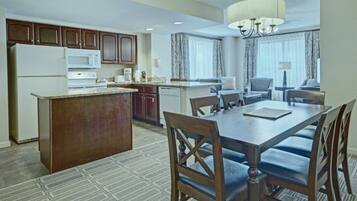 A hotel room with a dining area, kitchenette, and a large window with curtains.