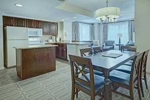 A hotel room with a dining area, kitchenette, and a large window with curtains.