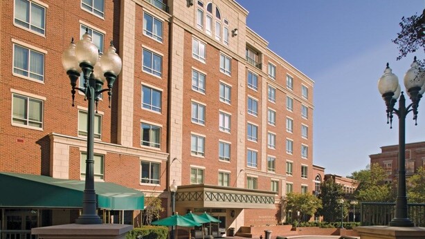 A multi-story brick building with a covered outdoor seating area and a gated entrance.