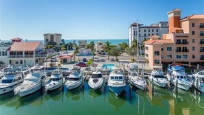 Un port de plaisance où sont amarrés de nombreux bateaux, entouré d’immeubles dotés de balcons et offrant une vue dégagée sur la mer.