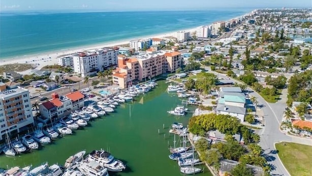 Un port de plaisance où sont amarrés de nombreux bateaux, entouré d’immeubles résidentiels et avec une plage en arrière-plan.