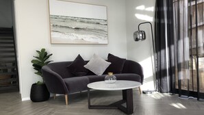 A modern living room with a dark-colored sofa, a round coffee table, and a large abstract painting on the wall. - Seaforth Retreat (Seaforth)