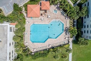 Ett flygbildsbild av ett semesterområde med en central pool, omgivet av palmer och avkopplande sittgrupper.