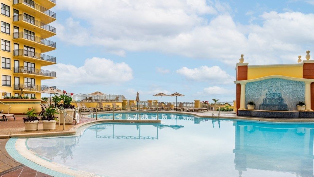 A swimming pool with lounge chairs and umbrellas, surrounded by a building with balconies.