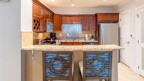 Una cocina con gabinetes de madera, encimera de granito, isla integrada con pileta y refrigerador.