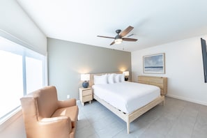 Ein Schlafzimmer mit Bett, Nachttischlampen, Deckenventilator, Nachttisch, Stuhl und einem Gemälde an der Wand.