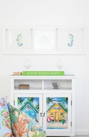 A white cabinet with a beach-themed artwork, a sign reading 'SUNSET BEACH PARTY,' and a colorful pillow.