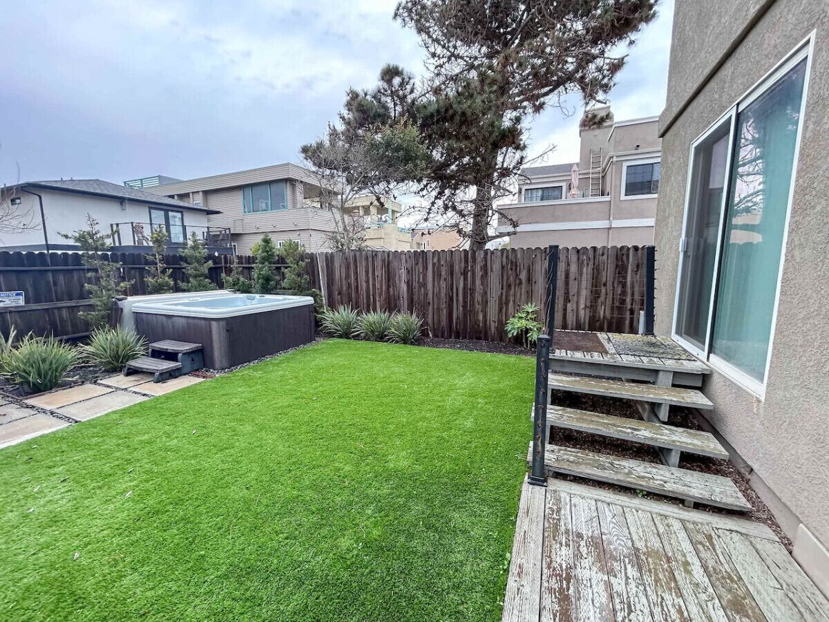 Een achtertuin met een verzorgd gazon, een jacuzzi en een houten terras.