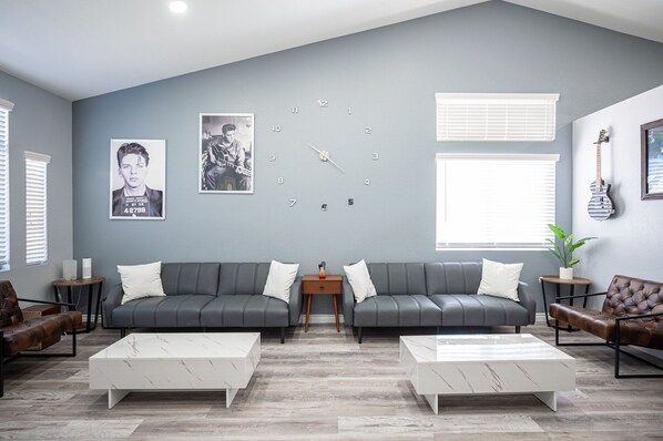 A modern living room with a grey sofa set, two white marble coffee tables, and a wall clock. - Luxury by the strip 5 star home close to LVB and airport. Great family home. (Henderson)