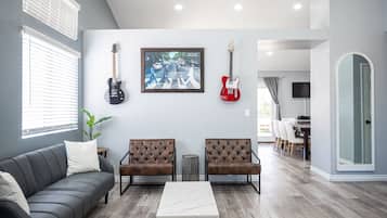 Een woonkamer met een grijze bank, twee bruine gestofte fauteuils, een witte salontafel, en twee gitaren aan de muur.