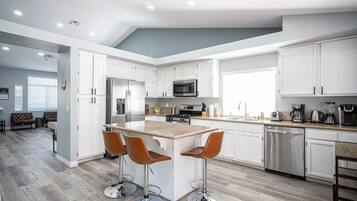 Een moderne keuken met witte kasten, roestvrijstalen apparatuur en een centraal eiland met barstoelen.