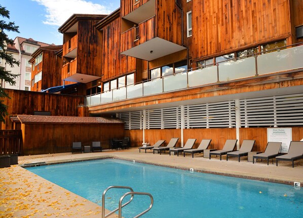 A pool area with lounge chairs, a pool ladder, and a sign indicating pool rules.