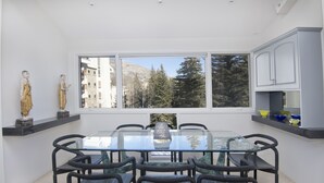 A modern dining area with a glass table and black chairs, a window with a view of trees and buildings, and a shelf with decorative items. - Ski-in/ski-out condominium at the base of Vail Mountain. Best location, pool!! (Vail)