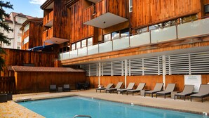 A pool area with a wooden deck, lounge chairs, and a pool with a metal ladder. - Ski-in/ski-out condominium at the base of Vail Mountain. Best location, pool!! (Vail)